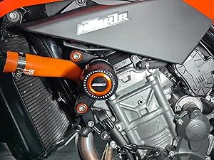 Détail rapproché d'un moteur de moto montrant des composants orange et noirs avec des finitions métalliques et des pièces mécaniques.
