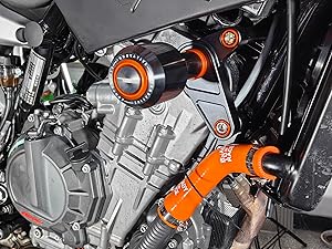 Images mécaniques rapprochées mettant en évidence différentes parties du moteur ou du système de transmission d'une motocyclette, avec des indicateurs circulaires oranges pointant vers des composants spécifiques.